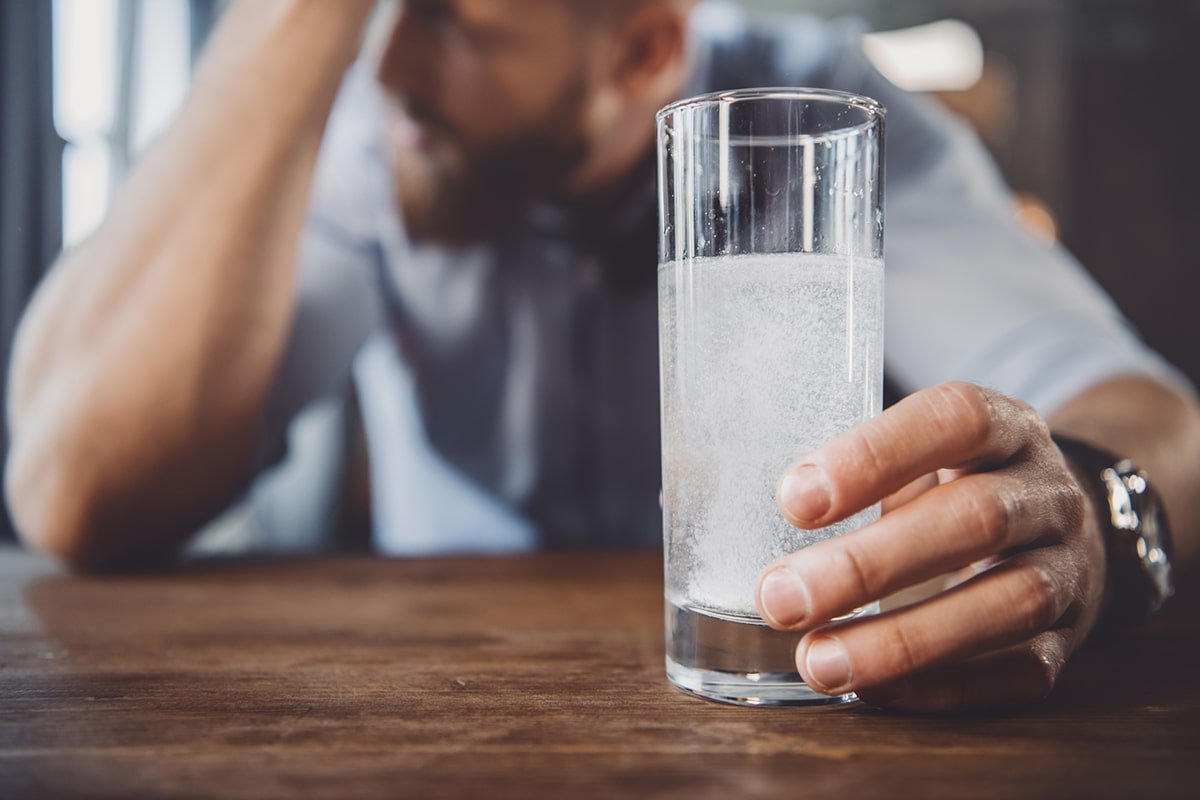 человек с похмельем держит стакан воды в руке